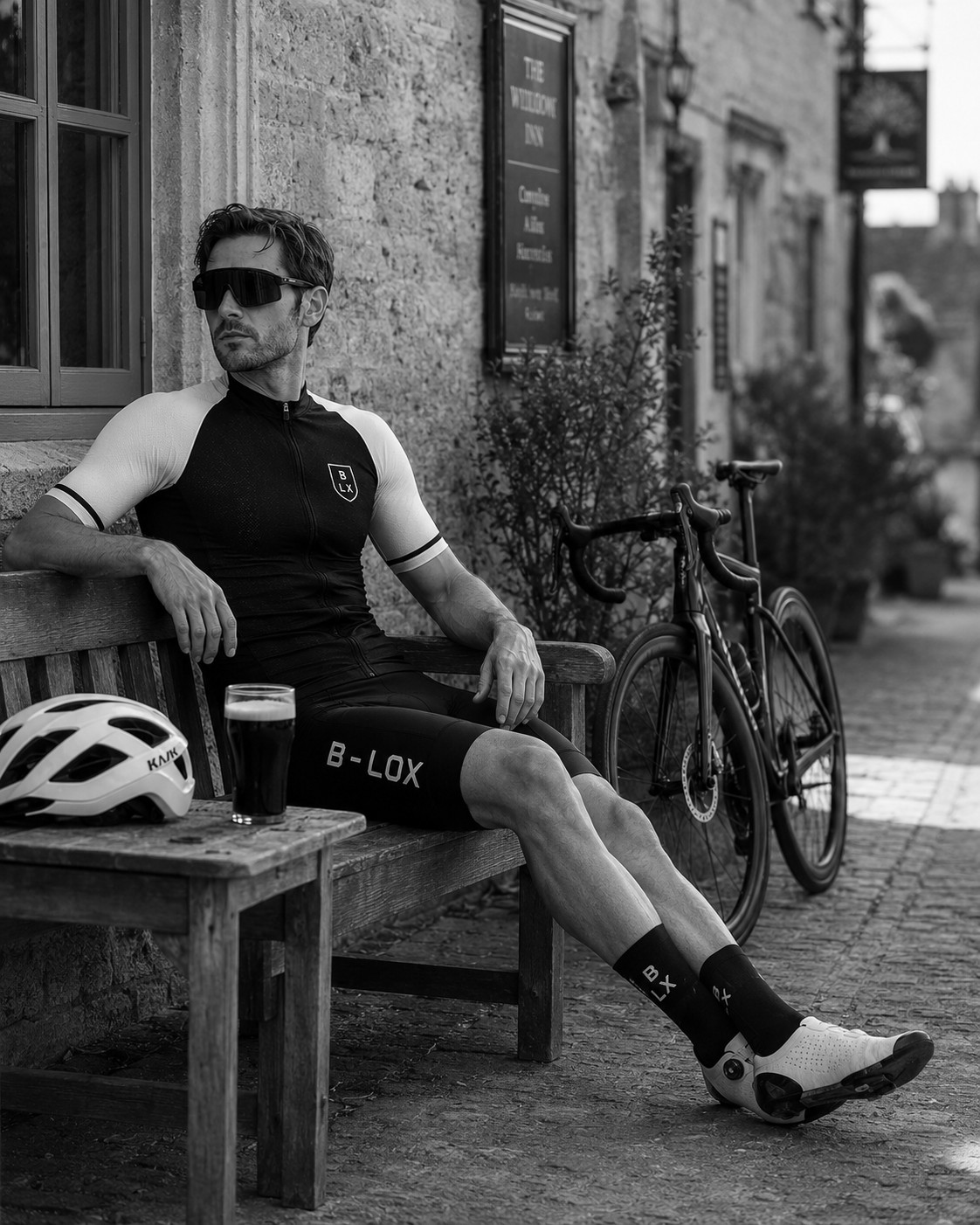 Rider in B-LOX kit sat on a bench outside a Cotswold pub, bike against the wall, pint on the table